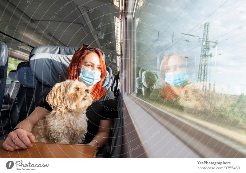 Junge Frau mit Gesichtsmaske und Hund reist mit dem Zug.Zugfahrt während der Pandemie Deutschland tausendjährig Abenteuer Business Class Wagen Kaukasier Stühle