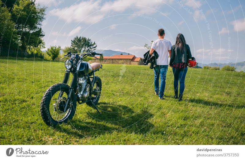 Paar, das auf dem Spielfeld geht und Hände und Motorrad hält unkenntlich rückwärts laufen geparkt Ausflug Mann Motorradhelm benutzerdefiniert verliebt