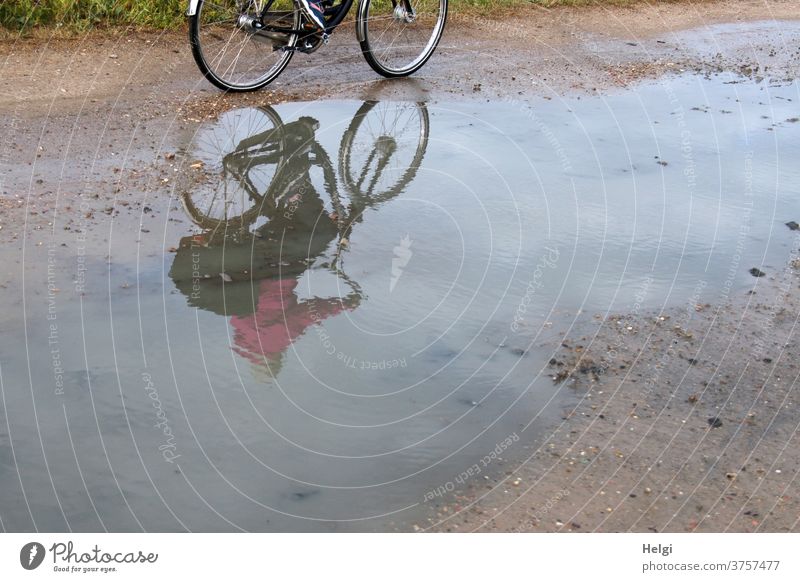 Radfahrerin gespiegelt in einer großen Pfütze auf einem Feldweg | dynamisch Fahrrad Fahrradfahrerin Spiegelung Natur Umwelt radeln Außenaufnahme