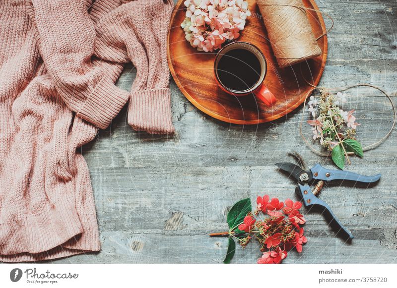Blick von oben auf den Herbst- oder Sommergarten mit gemütlichem Pullover, Kaffee, getrockneten Hortensienblüten und Gartenschneider Tisch Hintergrund Tasse