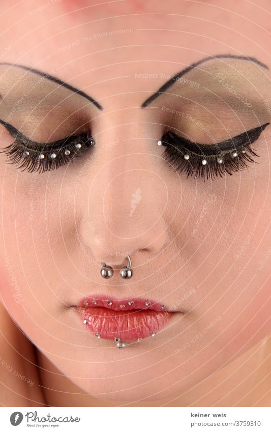 Ein geschminktes Frauengesicht in Nahaufnahme mit Nasenring und Piercing sowie Perlenschmuck auf Augen und Lippen Schmuck Gesichtsschmuck Körperschmuck Metall