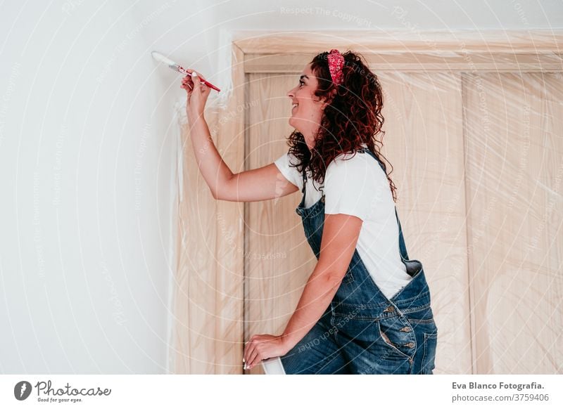 glückliche kaukasische Frau, die die Zimmerwände mit weißer Farbe streicht. Do it yourself und neues Wohnkonzept Kaukasier Malerei heimwärts Haus Bürste Glück