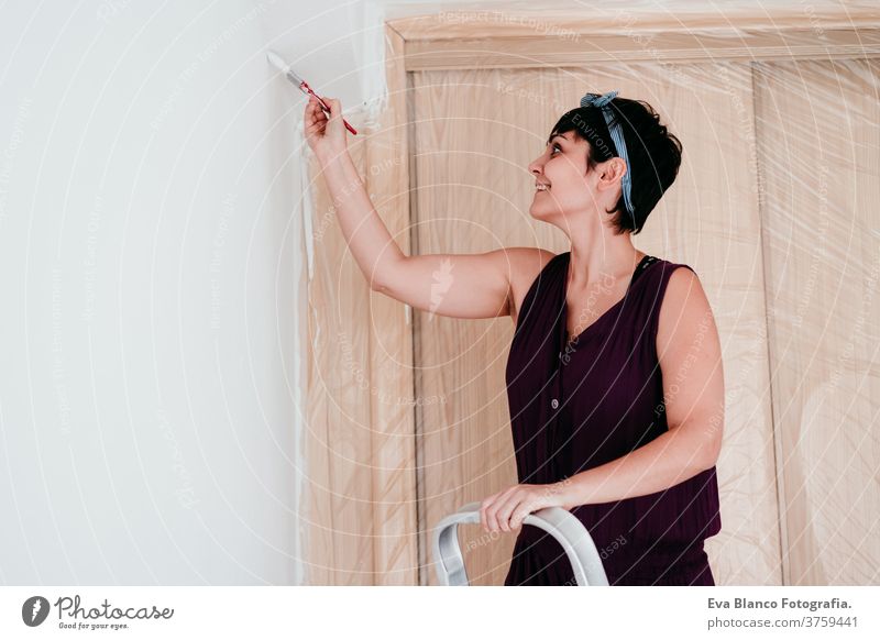 glückliche kaukasische Frau, die die Zimmerwände mit weißer Farbe streicht. Do it yourself und neues Wohnkonzept Kaukasier Malerei heimwärts Haus Bürste Glück