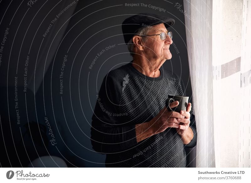 Älterer Mann lächelt aus dem Fenster Senior männlich Hut Brille heimwärts Glück Lächeln Blick Textfreiraum in den Ruhestand getreten Kaffee Becher Tasse Warten
