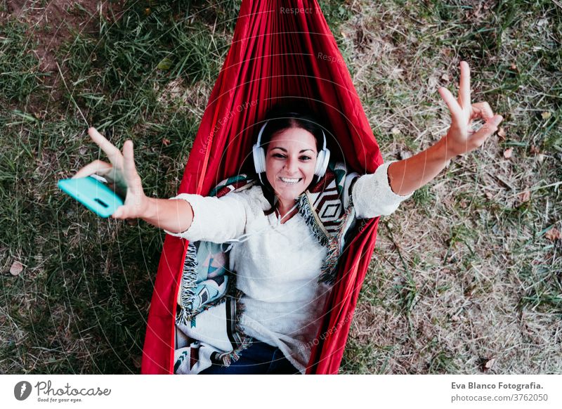 Draufsicht auf die glückliche Frau, die sich in der Hängematte entspannt und über Handy und Headset Musik hört. Herbstsaison. camping-Konzept Kopfhörer hören