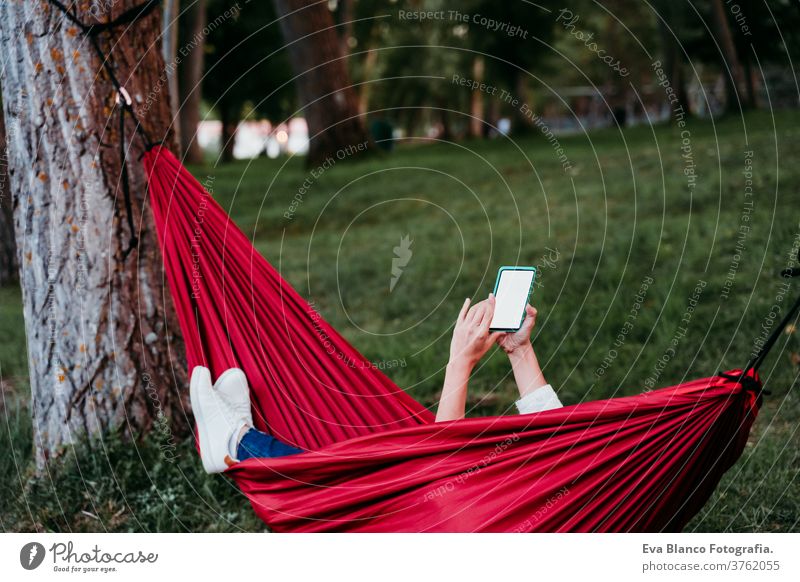 nicht erkennbare Frau, die sich in orangefarbener Hängematte mit dem Handy entspannt. Zelten im Freien. Herbstsaison bei Sonnenuntergang Headset Kopfhörer hören