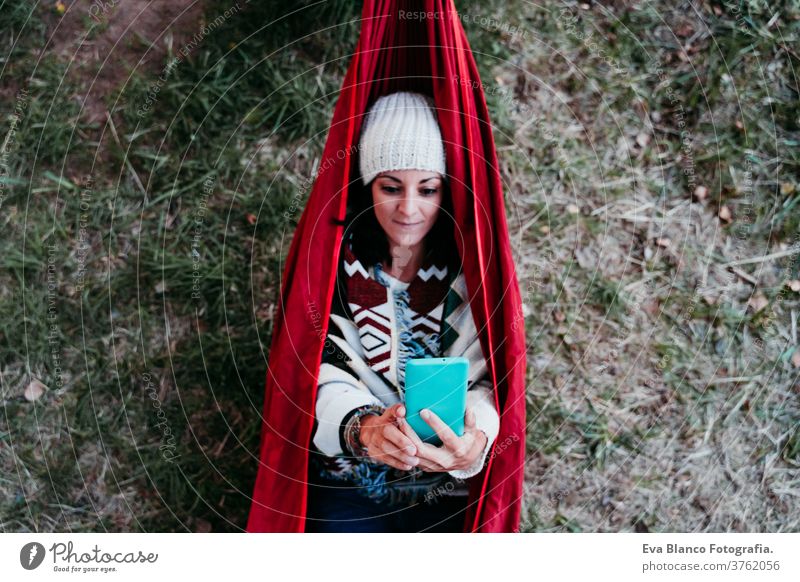 Draufsicht einer jungen Frau, die sich mit dem Handy in der Hängematte entspannt. Herbstsaison. Camping-Konzept Headset Kopfhörer hören Musik