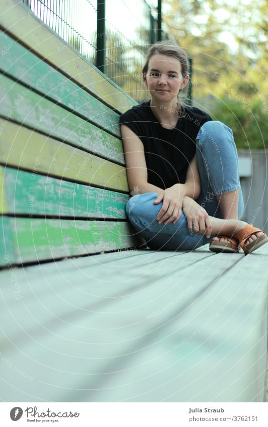 Frau sitzt auf einer langen Bank aus Holzbrettern sitzend zufrieden buisness lässig alternativ grün sozial Sommer Sandalen orange schwarz Streifen gestreift