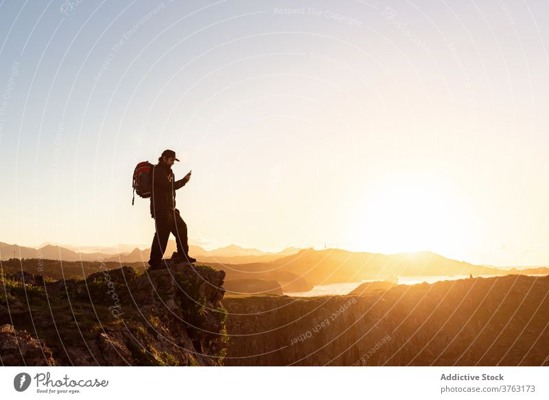 Reisender Mann, der den Sonnenuntergang mit seinem Smartphone fotografiert Hügel fotografieren benutzend Entdecker Rucksack Abenteuer männlich felsig Foto