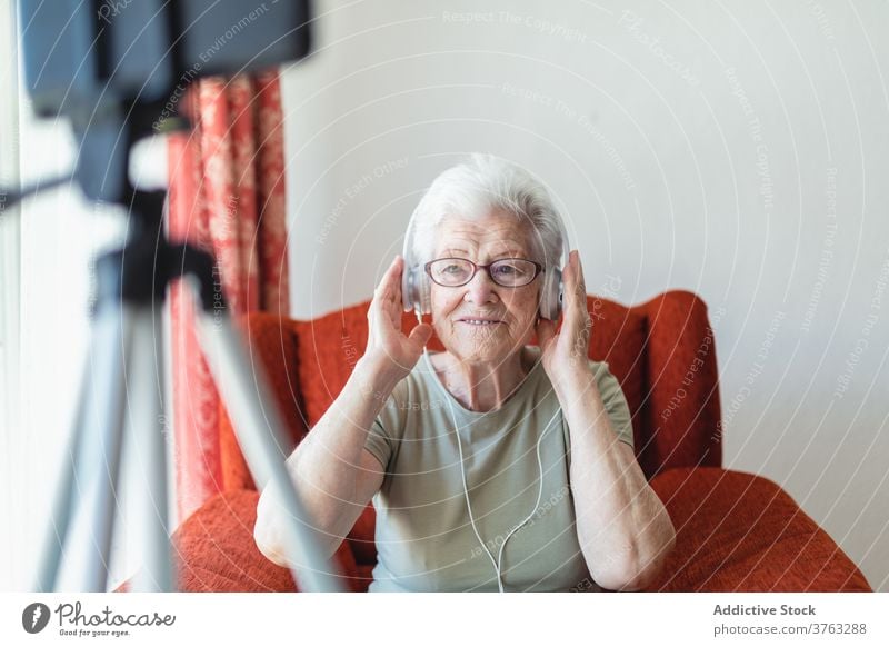 Lächelnde ältere Frau, die mit Kopfhörern Musik hört Senior zuhören Gesang genießen sich[Akk] entspannen heimwärts Freude Armsessel gemütlich sitzen heiter