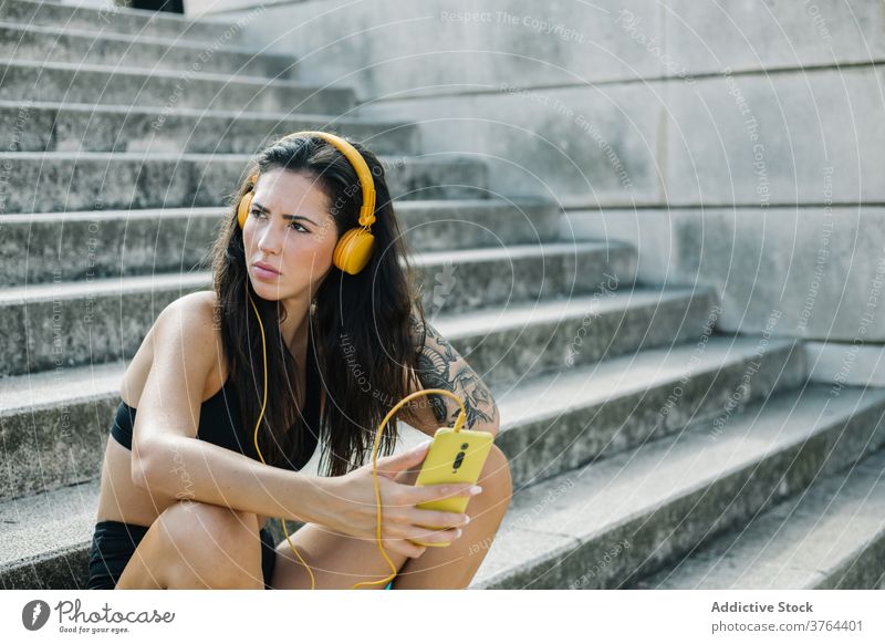 Seriöse Sportlerin beim Musikhören auf der Treppe Smartphone Kopfhörer zuhören ruhen Training Apparatur Athlet Frau benutzend Mobile Telefon Gerät