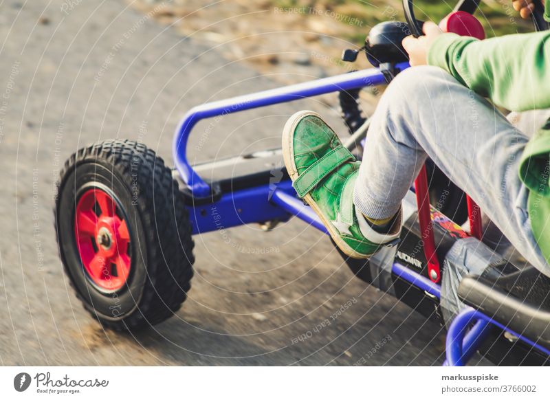Junge mit Vintage Retro Kettcar spielen Spielplatz Fahrzeug Vierrad Antrieb Fuß Bein Kraft Lenkrad Kindheit Abenteuer Spielplatzgeräte Spaß haben glücklich