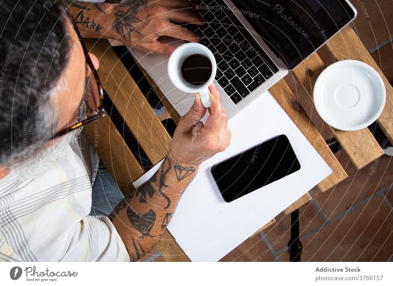 Beschäftigter Mann mit Tasse Kaffee arbeitet am Laptop Arbeit Arbeitsplatz beschäftigt benutzend Browsen trinken Apparatur Arbeit von zu Hause aus lässig