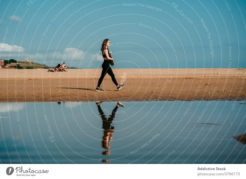 Frau mit Matte geht am Strand entlang Yogi Spaziergang Unterlage Sommer Sportbekleidung schlank sonnig Yoga Wasser Wellness Harmonie Fluss Flussufer Ufer