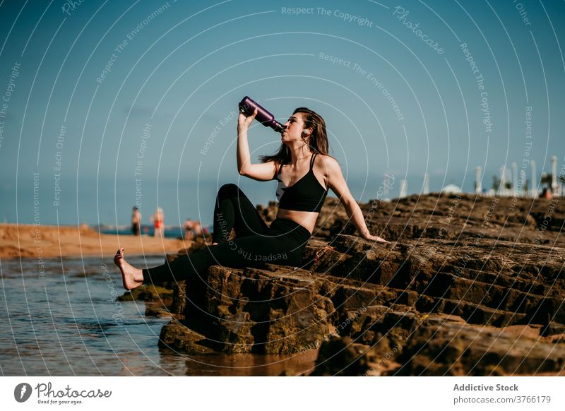 Ruhige Frau sitzt und trinkt Wasser nach Yoga trinken Ufer padmasana Zen Stressabbau Stein Sportbekleidung Wellness ruhig friedlich Harmonie üben