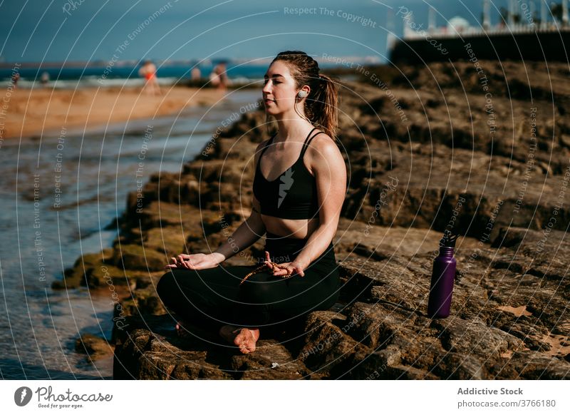 Tranquil Frau sitzt in Lotus-Pose und meditiert meditieren Yoga zuhören Kopfhörer Fluss Ufer padmasana Zen Stressabbau Achtsamkeit Stein Sportbekleidung