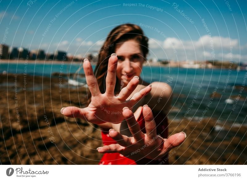 Lächelnde Frau zeigt Hände zur Kamera Anmut sich[Akk] melden Hand gestikulieren Meeresufer charmant Inhalt zeigen manifestieren sonnig Sommer Feiertag Küste