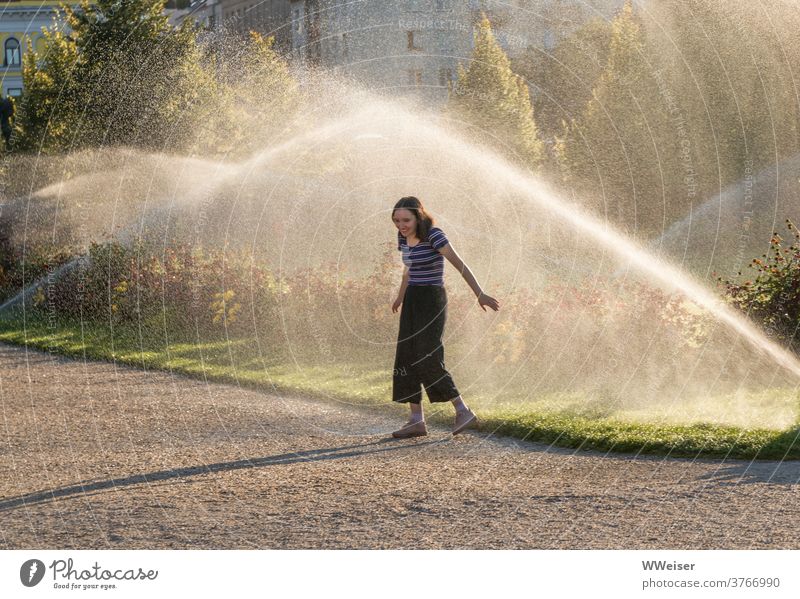 Eine Abkühlung im Sommer: eine junge Frau zwischen Schreck und Glück Rasensprenger Wasser erfrischend junges Mädchen sprühen sprengen Sonne Park Garten Augarten