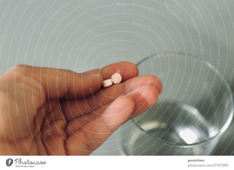 Eine Hand hält zwei Tabletten über einem Trinkglas. Medikamenteneinnahme, Gesundheitswesen medikament krankheit gesundheit depression psychische erkrankung