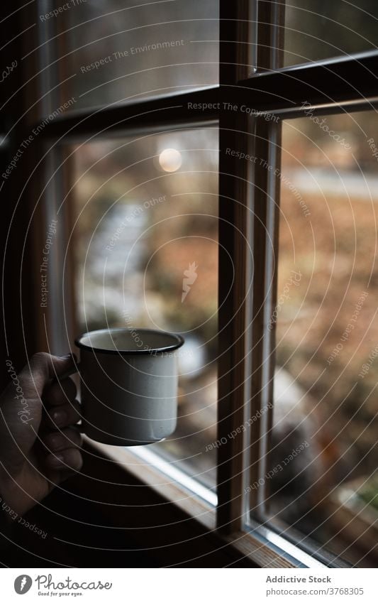 Anonyme Person genießt heißes Getränk in der Nähe von Fenster in kalten Herbsttag Heißgetränk Becher Landschaft Tasse Kaffee gemütlich Emaille reisen trinken