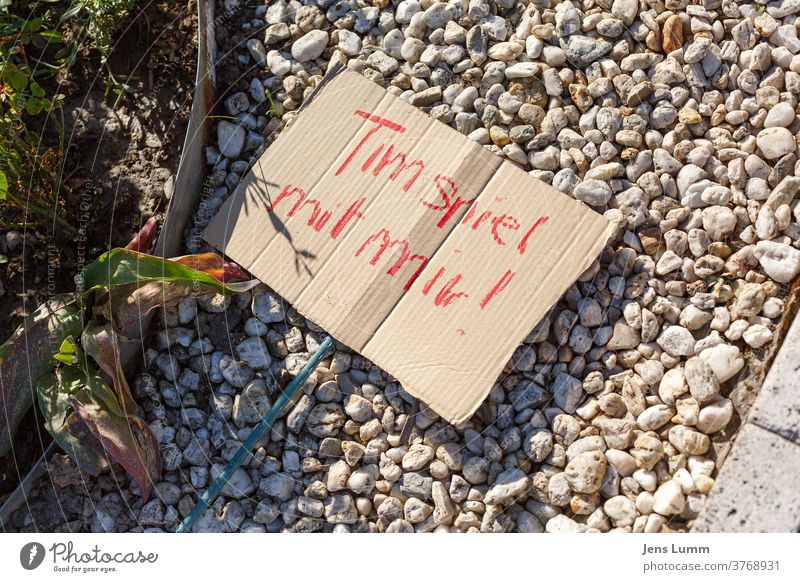 Ein Schild mit den Worten "Tim spiel mit mir!" Pappe rot Kiesbett Pflanze Garten Sommer spielende Kinder Spielen verboten corona Einsamkeit social distancing