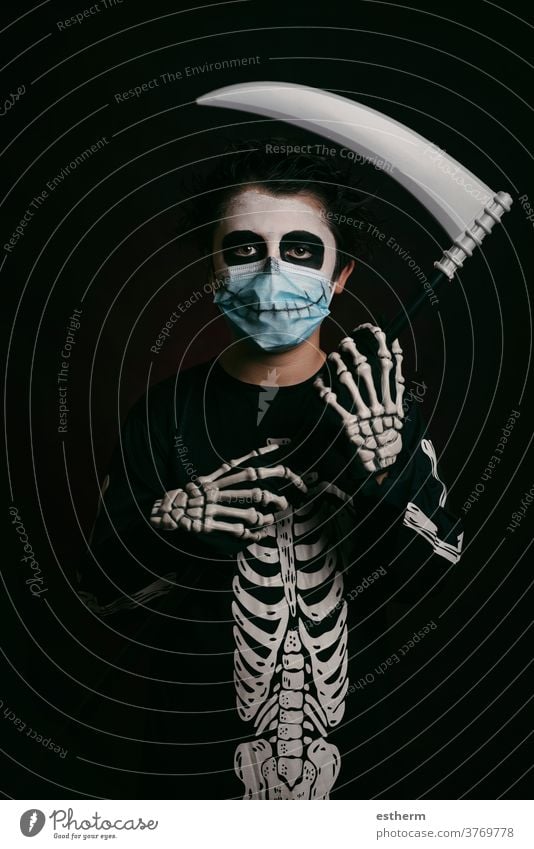 Happy Halloween,Kind mit medizinischer Maske in einem Skelettkostüm mit Sense medizinische Maske Coronavirus covid-19 Party Spaß Schädel Tracht Angst