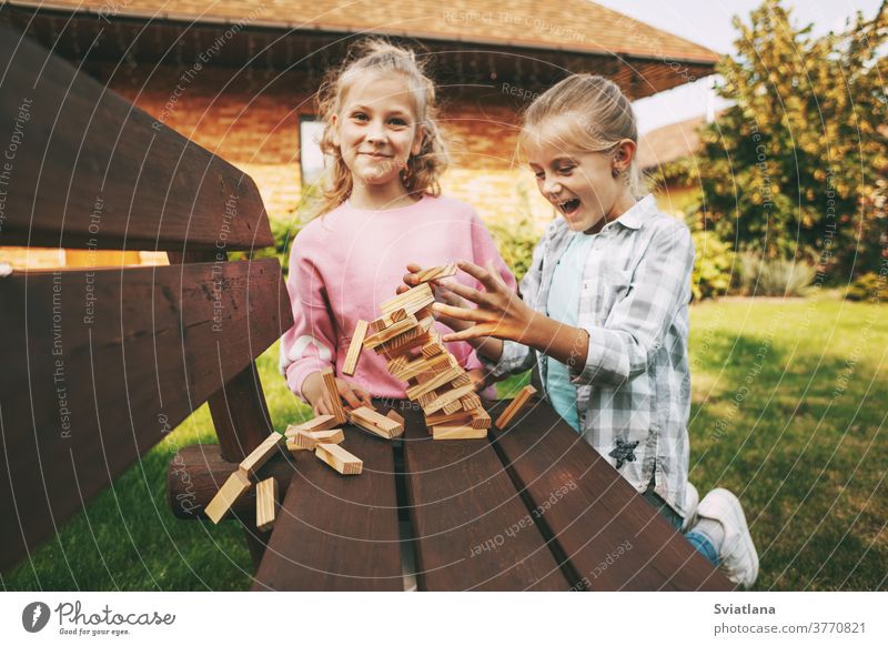Zwei Mädchen haben Spaß und spielen draußen in der Nähe ihres Hauses ein Holzbrettspiel. Spiel heimwärts Kinder Freizeit Entwicklung Baum Schwester drei Glück