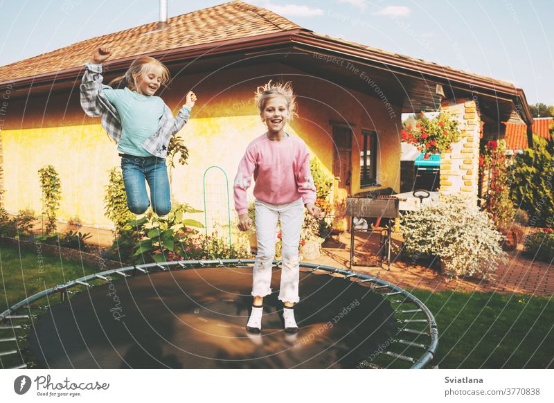 Glückliche zwei blonde Mädchen springen auf einem Trampolin im Garten in der Nähe ihres Hauses. Freizeit und Spiele Kinder Zusammensein Kindheit Kaukasier