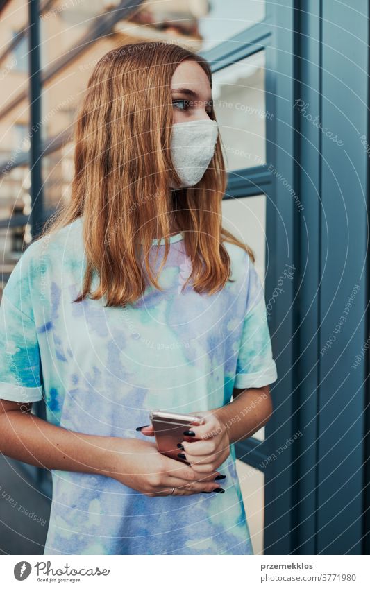 Porträt einer jungen Frau, die an der Ladenfront in der Innenstadt steht und eine Gesichtsmaske trägt, um eine Virusinfektion zu vermeiden Kaukasier Funktelefon