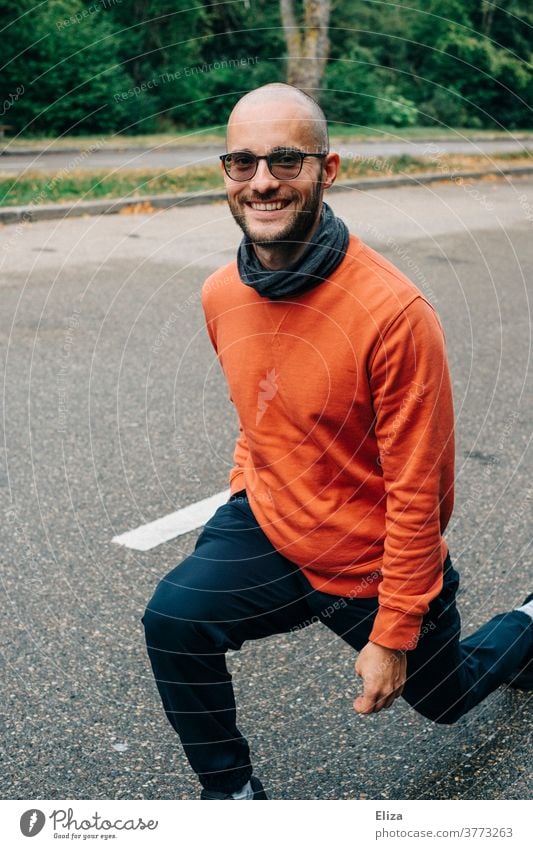Ein Mann macht Lunges (Ausfallschritte) auf einer Raststätte um sich in der Pause einer Autofahrt etwas zu bewegen Bewegung draußen zwischendurch Straße lächeln