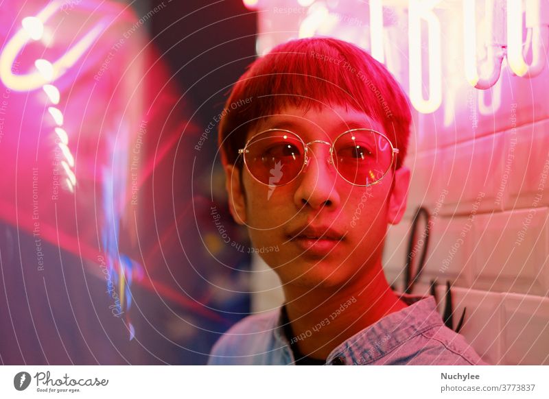 Junger asiatischer Hipster tausendjähriger Mann im Streetstyle-Modekonzept und mit Sonnenbrille in rosa Neonlicht Stilrichtung neonfarbig Jahrtausende gen z