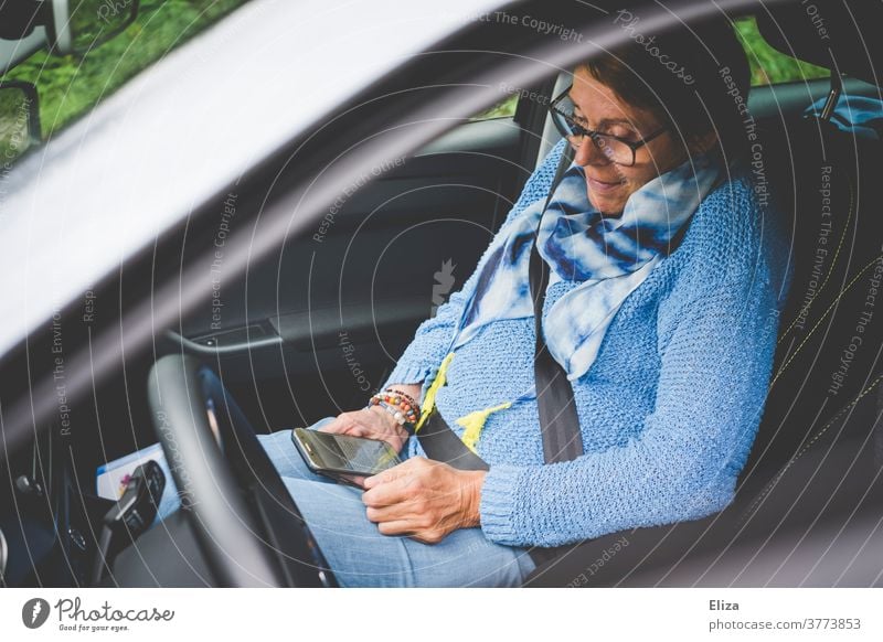 Eine Frau sitzt im Auto auf dem Beifahrersitz und sieht auf ihr Smartphone Handy sitzen benutzend beschäftigt Lächeln Telefon mobiltelefon Technik & Technologie