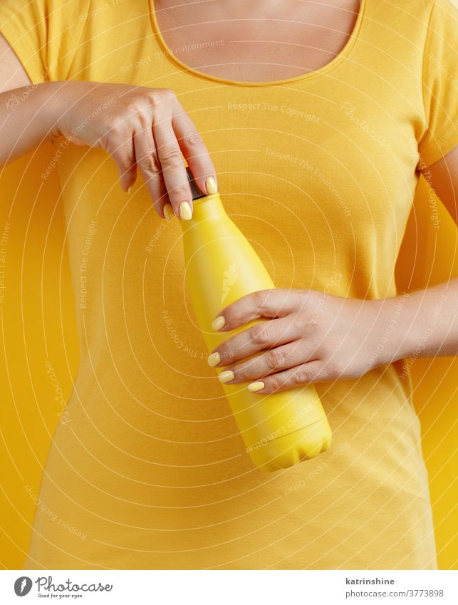 Nahaufnahme einer Frau, die eine gelbe wiederverwendbare Flasche auf gelbem Hintergrund hält Hand Monochrom ökologisch Wasser Stahl Thermo offen Halt hell