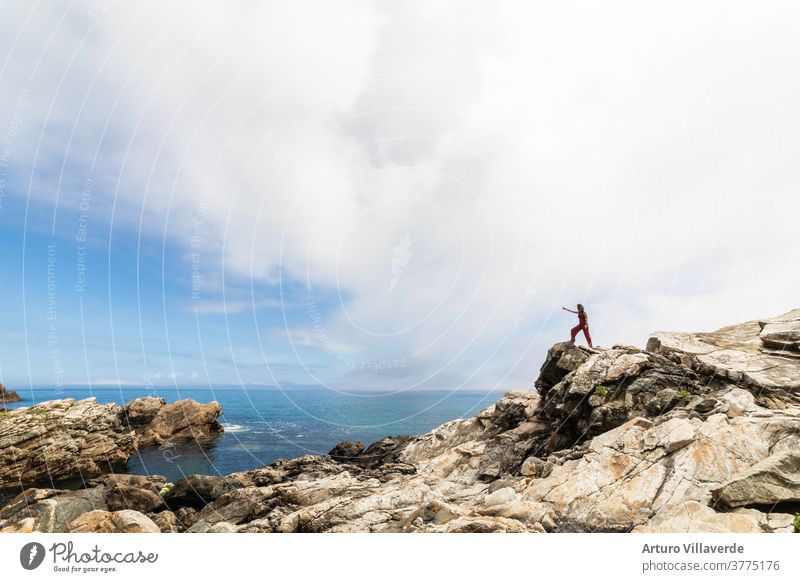 allgemeine Aufnahme der galicischen Küste mit einer Frau, die auf einigen Felsen sitzt und den Horizont beobachtet MEER Reisender Berge u. Gebirge Freiheit