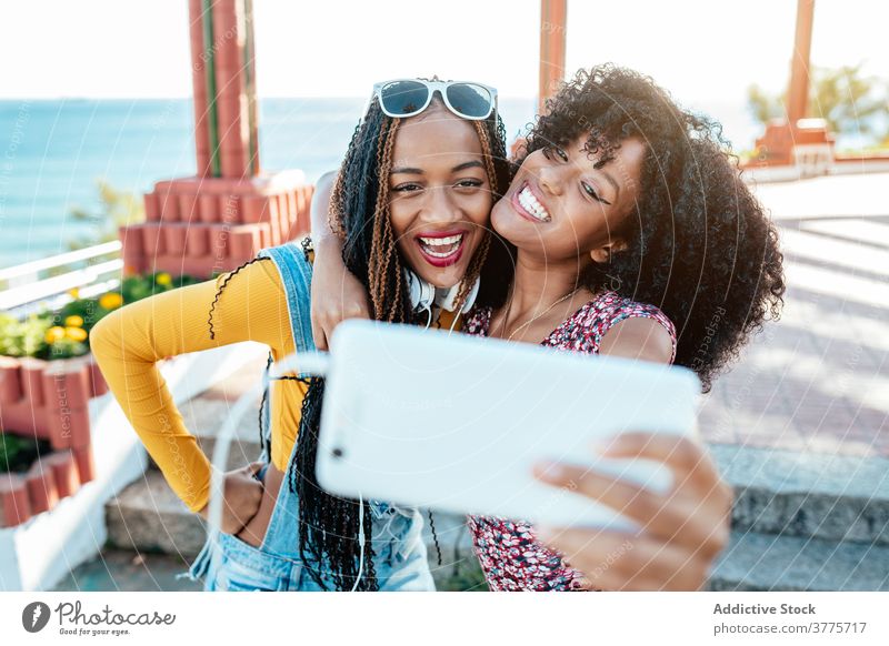 Fröhliche schwarze Freunde nehmen Selfie in der Stadt Umarmung Smartphone Frauen Freundschaft heiter Bonden benutzend Sommer Spazierweg ethnisch Afroamerikaner