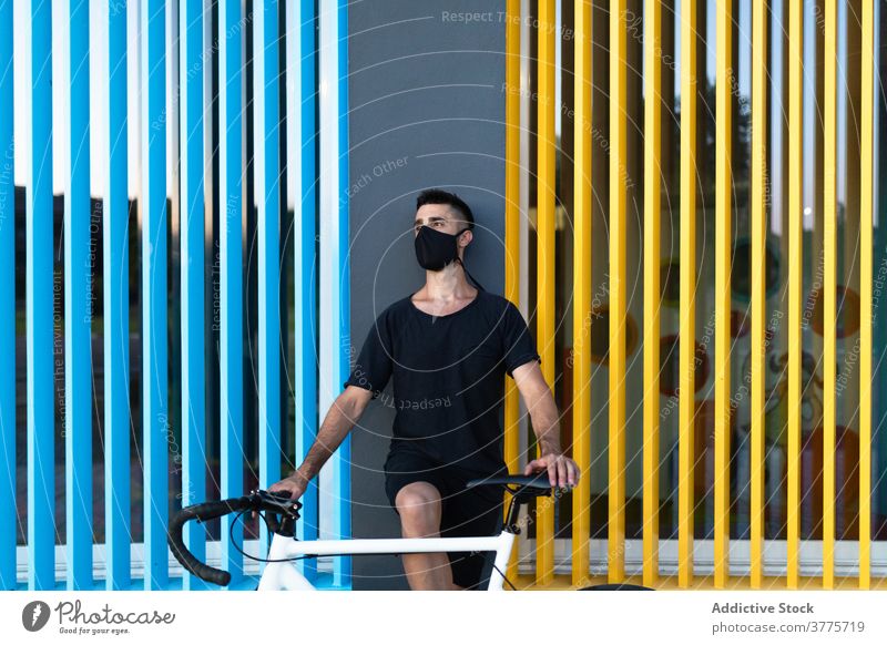 Mann in Maske mit Fahrrad auf der Straße Mundschutz Coronavirus Großstadt behüten Fahrzeug Seuche männlich farbenfroh Gebäude lebhaft pulsierend hell Farbe