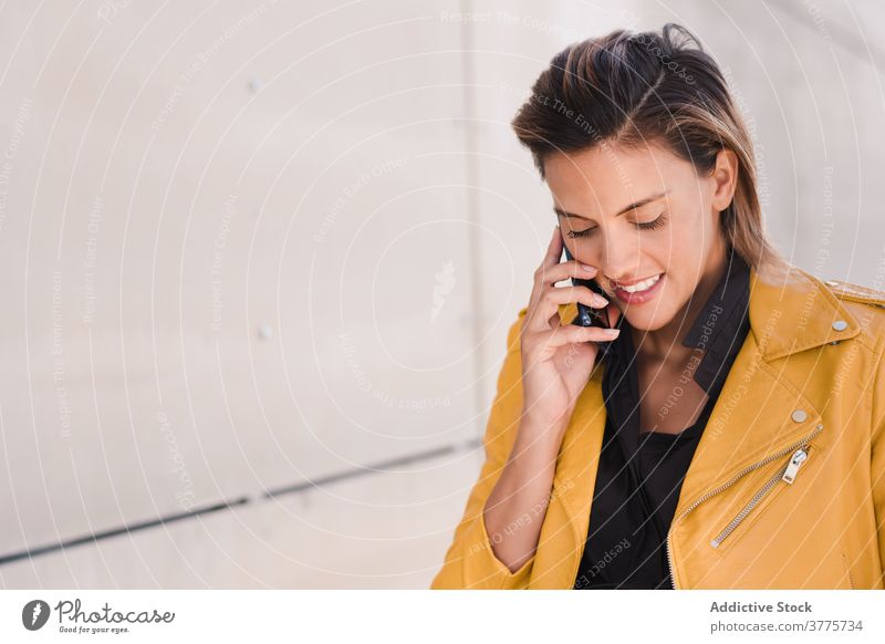 Lächelnde Frau spricht auf Smartphone in der Nähe von Gebäude sprechen reden Anruf Großstadt Funktelefon Gespräch benutzend Stil Inhalt Apparatur Gerät