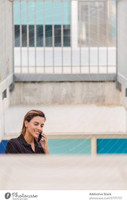 Lächelnde Frau spricht auf Smartphone in der Nähe von Gebäude sprechen reden Anruf Großstadt Funktelefon Gespräch benutzend Stil Inhalt Apparatur Gerät