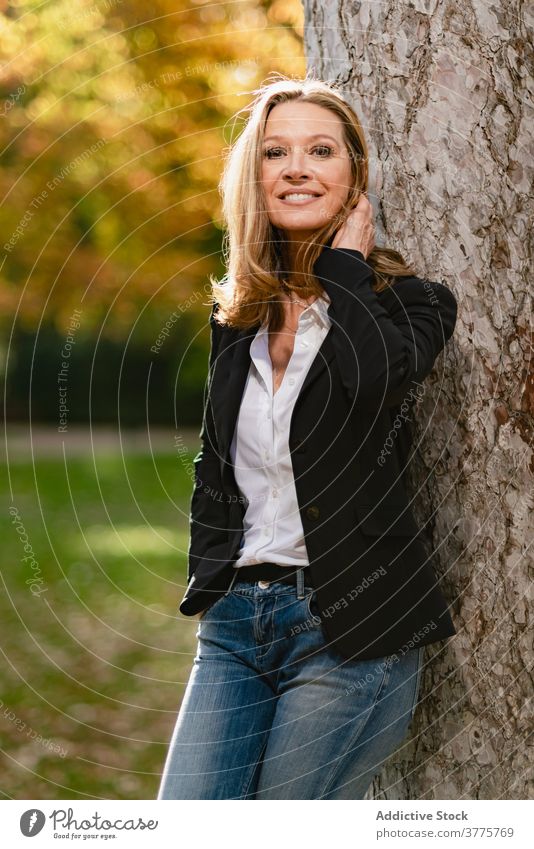 Lächelnde Frau in der Nähe von Baum im Park schlendern sich[Akk] entspannen genießen Saison Sonnenlicht Garten sorgenfrei Herbst fallen Stil Erholung Großstadt