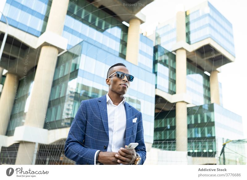 Seriöser Geschäftsmann steht in der Innenstadt Unternehmer Büro Gebäude Anzug Bestimmen Sie benutzend männlich ethnisch schwarz Afroamerikaner Glas formal