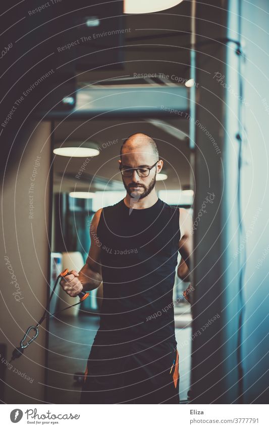 Ein Mann mit Bart und Brille beim Kraftsport im Fitnessstudio Rudern Anstrengung Sport Krafttraining muskulös Training Körper Übung sportlich stark Erwachsener