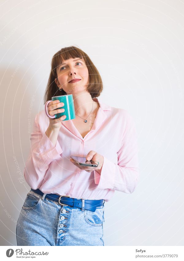 Frau, die Kaffee trinkt und ein Smartphone benutzt Wachtraum benutzend Gerät soziale Netzwerke Texten Handy Lächeln Tasse rosa modern jung trinken positiv
