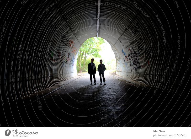 Silhouette zweier Jugendliche in einer Unterführung Tunnel Licht dunkel Graffiti Schatten Kontrast Bauwerk Architektur Wege & Pfade Fußgänger Lichterscheinung