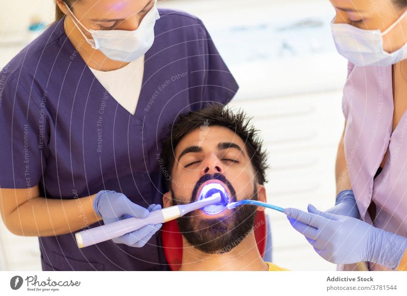 Zahnarzt und Assistentin heilen Zähne eines Mannes geduldig Klinik Aushärten Gerät Sog Licht Medizin Gesundheit dental Hygiene Behandlung männlich Frau Abfluss