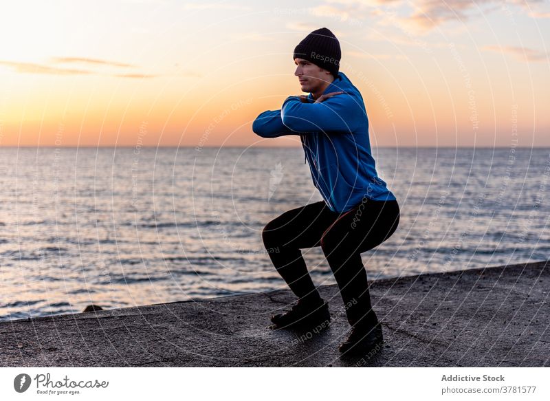 Sportler hockt auf der Stadtböschung Mann Training Kniebeuge MEER Fitness Übung Stauanlage sportlich urban Meer aktiv männlich ethnisch passen Gesundheit stark