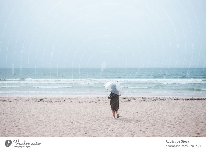 Anonyme Person mit Regenschirm, die am Sandstrand spazieren geht Strand MEER allein reisen Meer einsam stürmisch bedeckt Reisender Ufer Küste Natur winken