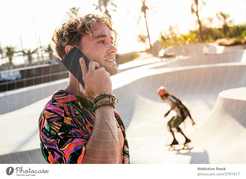 Fröhlicher Hipster, der im Skatepark mit seinem Smartphone spricht Skater Mann reden Stil trendy Kommunizieren Anruf Aktivität Rampe jung männlich Schlittschuh