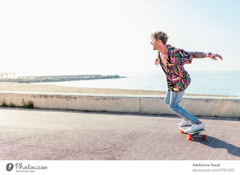 Unbeschwerter Mann fährt Skateboard entlang der Promenade Skater Sommer Hipster Stauanlage Schlittschuh Wochenende Gleichgewicht Fähigkeit männlich Stil trendy
