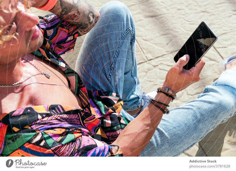 Junger trendiger Mann mit Smartphone im Park Hipster Lächeln soziale Netzwerke jung trendy benutzend Nachricht männlich Mobile Gerät sonnig Telefon Browsen