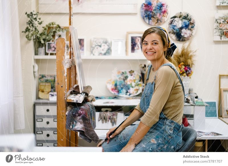 Glückliche Handwerkerin malt auf Staffelei in Werkstatt Frau Künstler Farbe Leinwand heiter kreativ zeichnen Lächeln Kunst Talent Arbeit farbenfroh Bild Hobby
